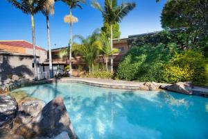 a swimming pool with palm trees in a yard at Villa Noosa Hotel in Noosaville