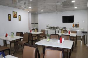 uma sala de jantar com mesas e cadeiras brancas em Hotel The Furat Inn em Vapi