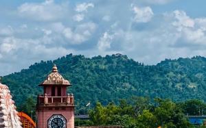uma torre de relógio com uma montanha ao fundo em Hotel ShivMurti Classic em Haridwar