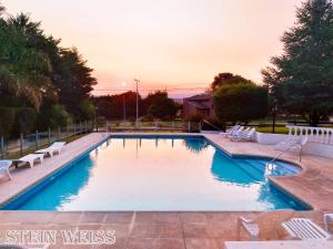 uma piscina com cadeiras brancas e um pôr-do-sol em Cabañas Stein Weiss em Santa Rosa de Calamuchita
