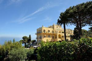 a yellow building with a palm tree in front of it at Hotel Caesar Augustus in Anacapri