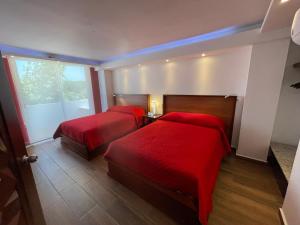 two beds in a room with red sheets and a window at La Mansión del Faro in Tecolutla