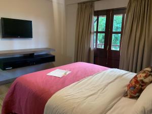 a hotel room with a bed with a tv and a window at Flor de Café Pousada in Pedra Menina