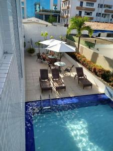 uma piscina com cadeiras, uma mesa e um guarda-sol em Flat 406- Imperial Flat Tambaú NOBILE em João Pessoa