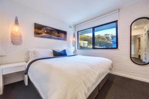 a white bedroom with a large bed and a mirror at Snow Ski Apartments Penthouse 33 in Falls Creek
