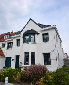 uma casa branca com janelas pretas e arbustos em Villa La Croisée des Chemins em Bray-Dunes