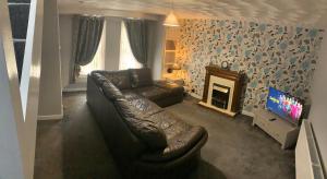 een woonkamer met een leren bank en een televisie bij 1-2 Dialknowe Holiday Cottage - Wanlockhead in Wanlockhead