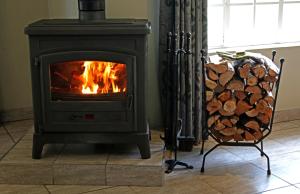 a wood stove with a chair and a pile of logs at Copperleigh Trout Cottages in Dargle