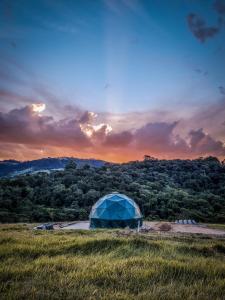 a tent in a field with a sunset in the background at Domo da Cuesta - Glamping com vista para a montanha in Bofete