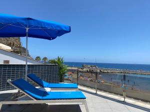 two blue lounge chairs and an umbrella on a balcony with the beach at Billy's Beachfront Apartment with pool access in Puerto de Mogán