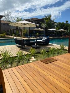 una terraza de madera con mesa y sombrilla junto a la piscina en Flat luxo, próximo da praia e da vila de Barra Grande-Ba na península de Maraú - Condomínio Villagio de Mari, en Maraú