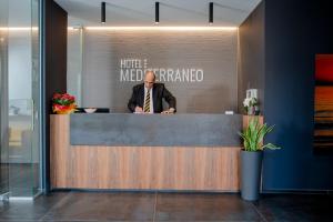 Um homem está sentado na recepção. em Hotel Mediterraneo -Spiaggia Ombrelloni e Lettini Inclusi- em Martinsicuro
