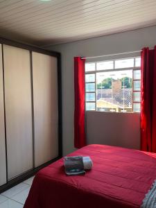 a bedroom with a bed with red sheets and a window at Quarto Privado em residência no Coração de Foz - casa e banheiro compartilhado in Foz do Iguaçu