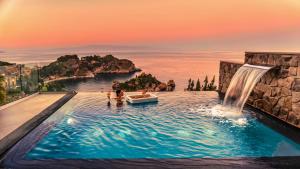 una piscina con cascada y un barco en el agua en Isola Bella Infinity Suites en Taormina