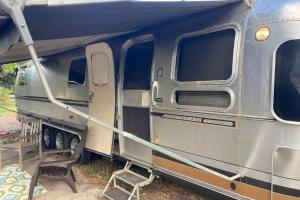 un remolque azul y plateado con una silla al lado en Beautiful Airstream, Beaufort SC-Enjoy the Journey en Beaufort