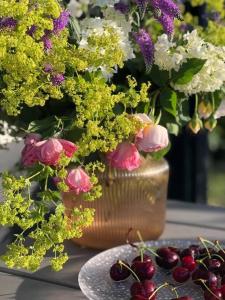 wazon wypełniony kwiatami i wiśniami na stole w obiekcie Ragaciema Skadiņi w mieście Ragaciems