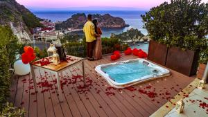 two people standing on a deck with a hot tub at Isola Bella Infinity Suites in Taormina