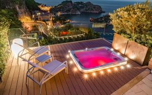 a hot tub on a deck with two chairs and lights at Isola Bella Infinity Suites in Taormina