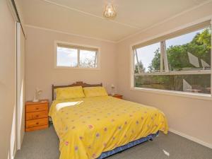 a bedroom with a bed with a yellow comforter and a window at Hosts on the Coast Whiti Delight in Whitianga