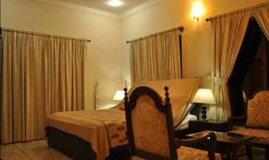 ein Schlafzimmer mit einem Bett, einem Stuhl und Vorhängen in der Unterkunft Sarai Silk Route in Islamabad