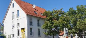 a white building with a red roof next to a tree at Outletcity Ferienwohnung Wohnung 2 in Metzingen