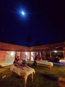 een groep mensen die 's nachts op tafels zitten bij Pousada Casa de João Kitehouse in São Miguel do Gostoso