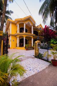 a yellow house with a gate and palm trees at Primavera Holiday Homes-GOA-CANDOLIM BEACH WITHIN 300 MTRS-GOAN FAMILY HOSPITALITY in Candolim