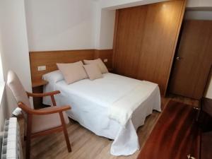 Un pequeño dormitorio con una cama blanca y una silla en Casa en el centro histórico de Corcubión., en Corcubión