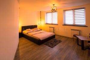 a bedroom with a bed and a table and two windows at Apartament Izabel in Nowy Targ