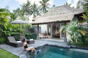 a woman sitting next to a swimming pool in a villa at The Sun of Granary Resort and Villas in Ubud