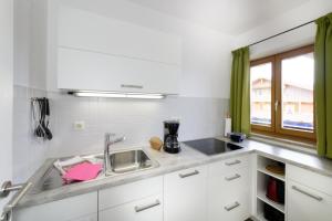 biała kuchnia ze zlewem i oknem w obiekcie Ferienwohnungen Trinkl w mieście Bad Wiessee