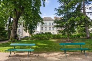 zwei Bänke in einem Park mit einem Gebäude im Hintergrund in der Unterkunft Résidence de Tourisme Central Parc Tours in Tours