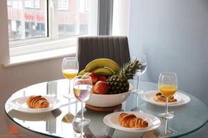 a glass table with a bowl of fruit and glasses of wine at Modern Newgate Apartments - Kingsbury Underground, All Local Amenities on Your Doorstep in Wealdstone