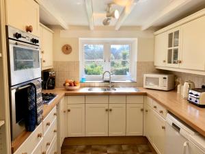 cocina con armarios blancos, fregadero y ventana en Tresowes Green Cottage, en Helston