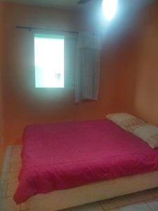 um quarto com uma cama com um cobertor vermelho e uma janela em Casa 50 mts da praia Caravelas PR com ventiladores em Matinhos