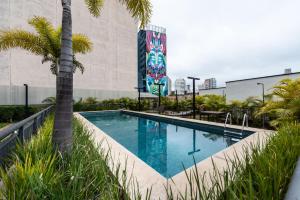 uma piscina com uma palmeira ao lado de um edifício em "Book Your Stay at Homelike Faria Lima in Pinheiros Stunning City Views Pool and Parking by Okaeri Home em São Paulo