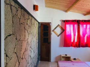 Habitación con cortinas rojas y pared de piedra. en Pedra de Rala, en Porto Novo