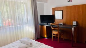 a hotel room with a desk with a television and a bed at Pensiunea Kalinder in Buşteni