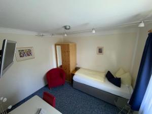 Habitación pequeña con cama y silla roja. en Hotel Sonnenspitz ***, en Kochel