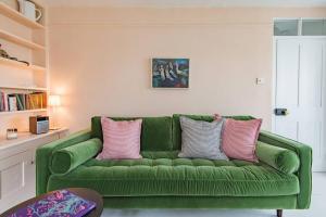 ein grünes Sofa im Wohnzimmer mit rosa Kissen in der Unterkunft Trafalgar Cottage - Stunning sea view property on beach in Kingsdown