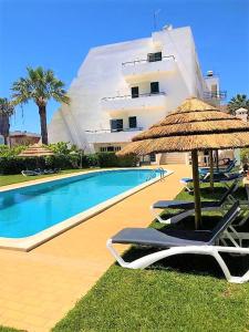 a pool with chairs and an umbrella and a building at Debimar Apartamentos in Albufeira