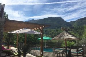 a patio with a pool and umbrellas and a view of mountains at Petit 2P au coeur des montagnes in Puget-Théniers