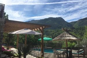 a patio with a pool and umbrellas and a view of mountains at 2P au coeur des montagnes avec piscine chauffée in Puget-Théniers