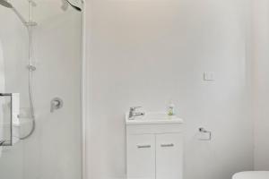uma casa de banho branca com um chuveiro e um lavatório. em Karori Kabin - Karori Holiday Home em Wellington