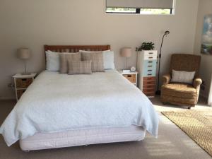 ein Schlafzimmer mit einem weißen Bett und einem Stuhl in der Unterkunft Abel Tasman Sands BnB in Marahau