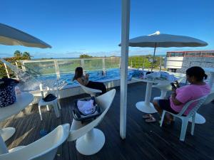 two women sitting at tables on a deck with a pool at Israel Flat Tambaú in João Pessoa
