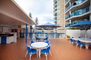 un patio con mesas, sillas y sombrillas azules en Grosvenor Beachfront Apartments Surfers Paradise en Gold Coast