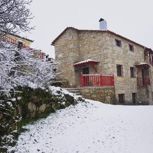 un bâtiment en pierre avec un portail rouge dans la neige dans l'établissement Casas Da Ribeira, à Seia