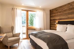 a bedroom with a bed and a chair and a window at Typically Swiss Hotel Ermitage in Kandersteg