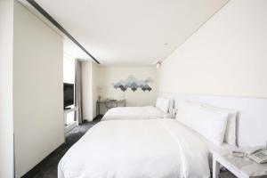 a white bedroom with two beds and a tv at Ambience Hotel Taipei in Taipei